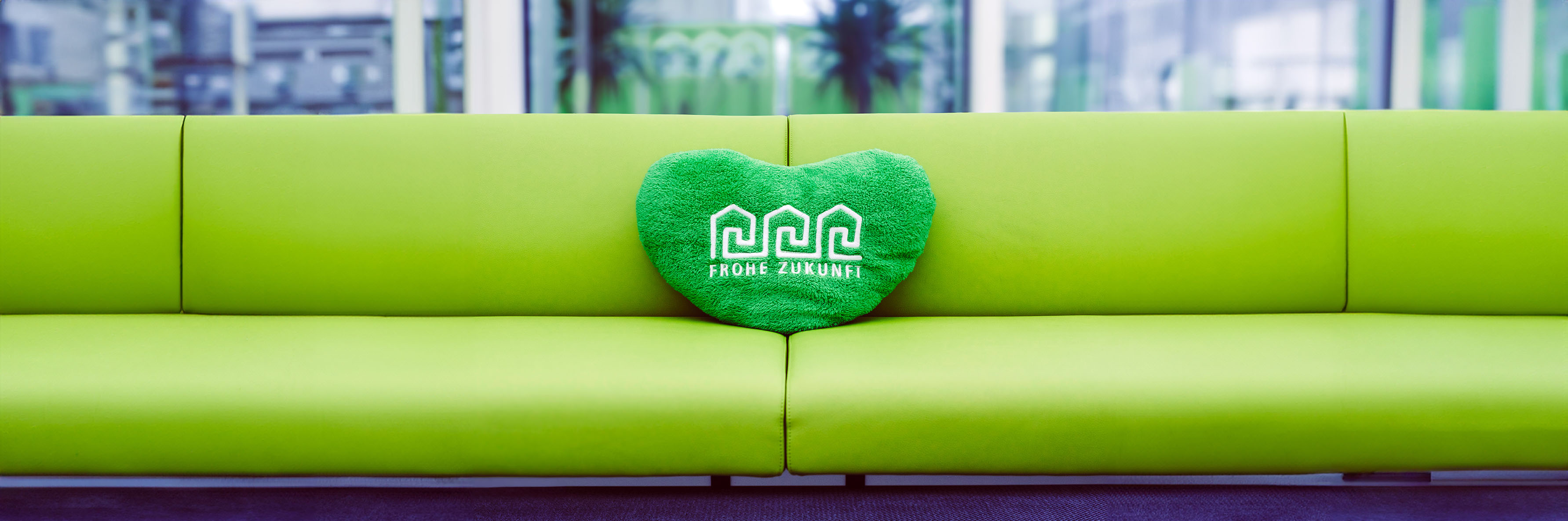 Header Grüne Couch mit Herz-Stoffkissen der FROHE ZUKUNFT Wohnungsgenossenschaft
