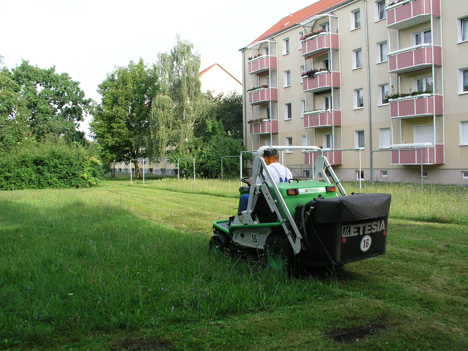 jemand fährt einen Rasentraktor und mäht eine Wiese vor einem Wohnhaus