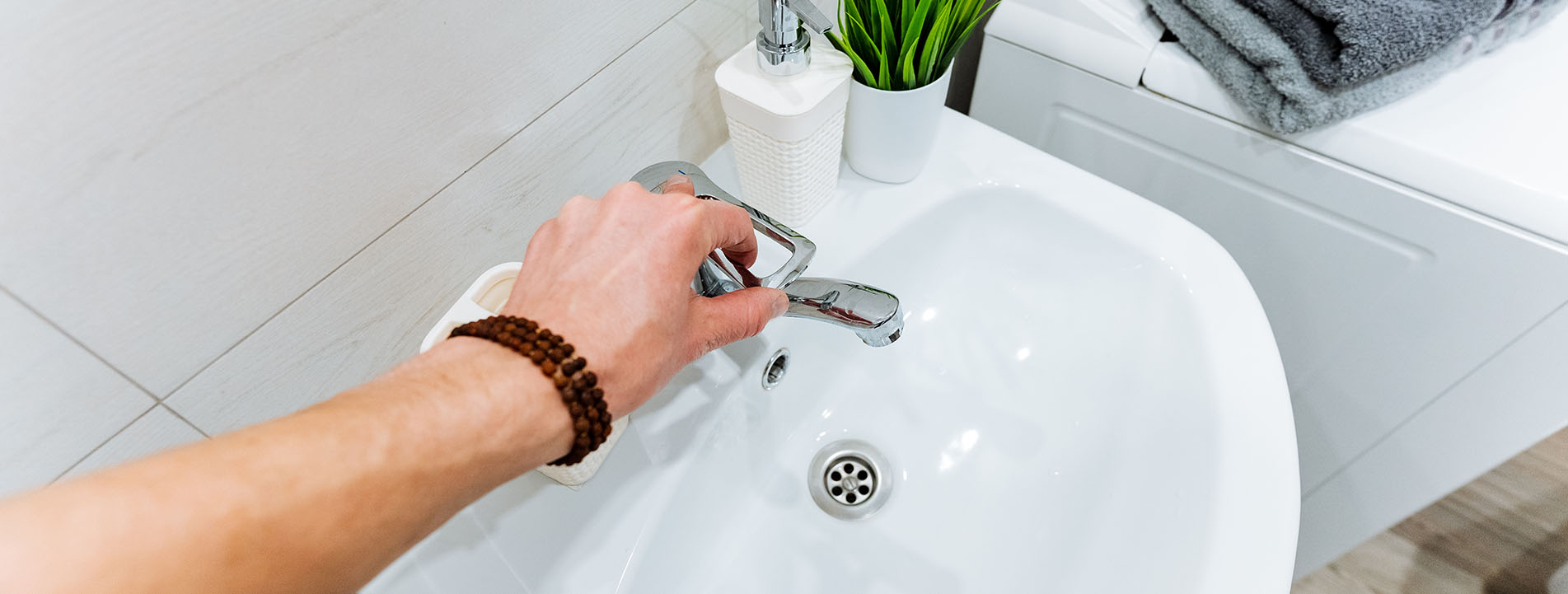 Foto Hand öffnet Wasserhahn am weißen Waschbecken neben Waschmaschine im Badezimmer